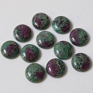 May include: A collection of eleven round gemstones. Each stone features a mottled pattern of deep red and green hues. The gemstones are polished and have a smooth, reflective surface, suggesting they are cabochons, suitable for jewelry making or crafts.