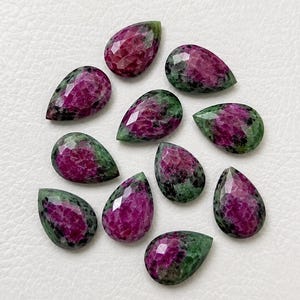 May include: A collection of ten pear-shaped ruby zoisite gemstones. Each stone features a faceted surface with a distinct colour combination of deep magenta-pink ruby inclusions contrasted against a dark forest green zoisite mineral matrix.
