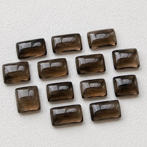 Pode incluir: Uma coleção de doze pedras preciosas de quartzo fumê retangulares. Cada pedra tem uma superfície polida e brilhante, com uma rica cor marrom. As pedras preciosas estão dispostas sobre uma superfície branca, mostrando sua clareza e forma.