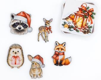 May include: A set of five wooden animal cutouts including a raccoon in a Santa hat, a fawn with a red bow, a hedgehog holding a gift, a rabbit in a Santa hat, and a fox in a scarf, alongside a square tin featuring a lantern and robin.