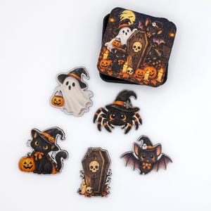 May include: A set of five Halloween-themed wooden magnets and a square storage tin. The designs feature a white ghost with a pumpkin, a spider in a witch hat, a black cat with a pumpkin, a coffin with a skull, and a bat with a bow.