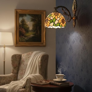 May include: A wall-mounted Tiffany-style lamp with a sunflower design. The lamp features a stained glass shade with yellow, green, and white panels. The lamp is mounted on a dark metal arm and bracket. A painting, armchair, and side table with a cup of tea are also visible.