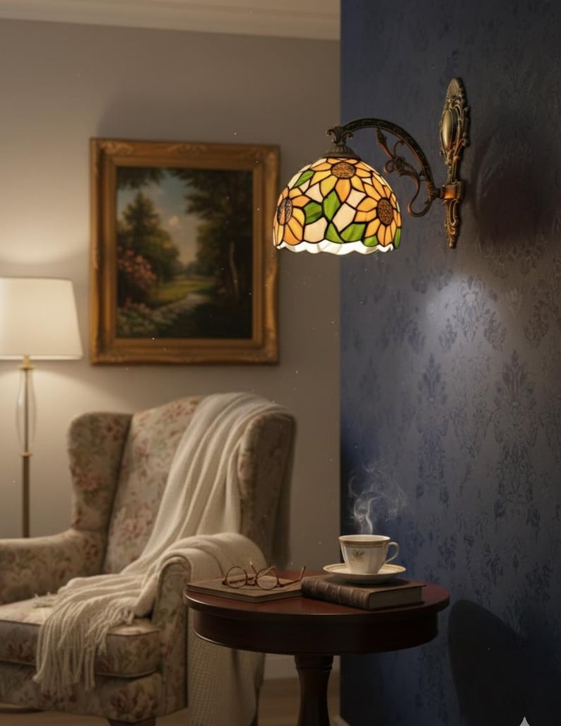 May include: A wall-mounted Tiffany-style lamp with a sunflower design. The lamp features a stained glass shade with yellow, green, and white panels. The lamp is mounted on a dark metal arm and bracket. A painting, armchair, and side table with a cup of tea are also visible.