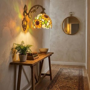 May include: A wall-mounted lamp with a stained glass shade featuring a sunflower design. The lamp has a bronze-colored metal arm and base. A wooden console table with books, a plant, and a bowl is below the lamp. A decorative rug is on the floor.