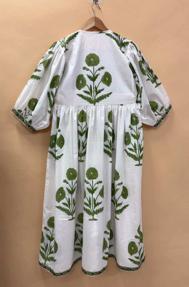 Puede incluir: Vestido blanco con estampado floral verde. El vestido presenta un cuello redondo, mangas cortas y cintura fruncida. El dise&ntilde;o floral verde se repite, con ribete verde en las mangas y el dobladillo.