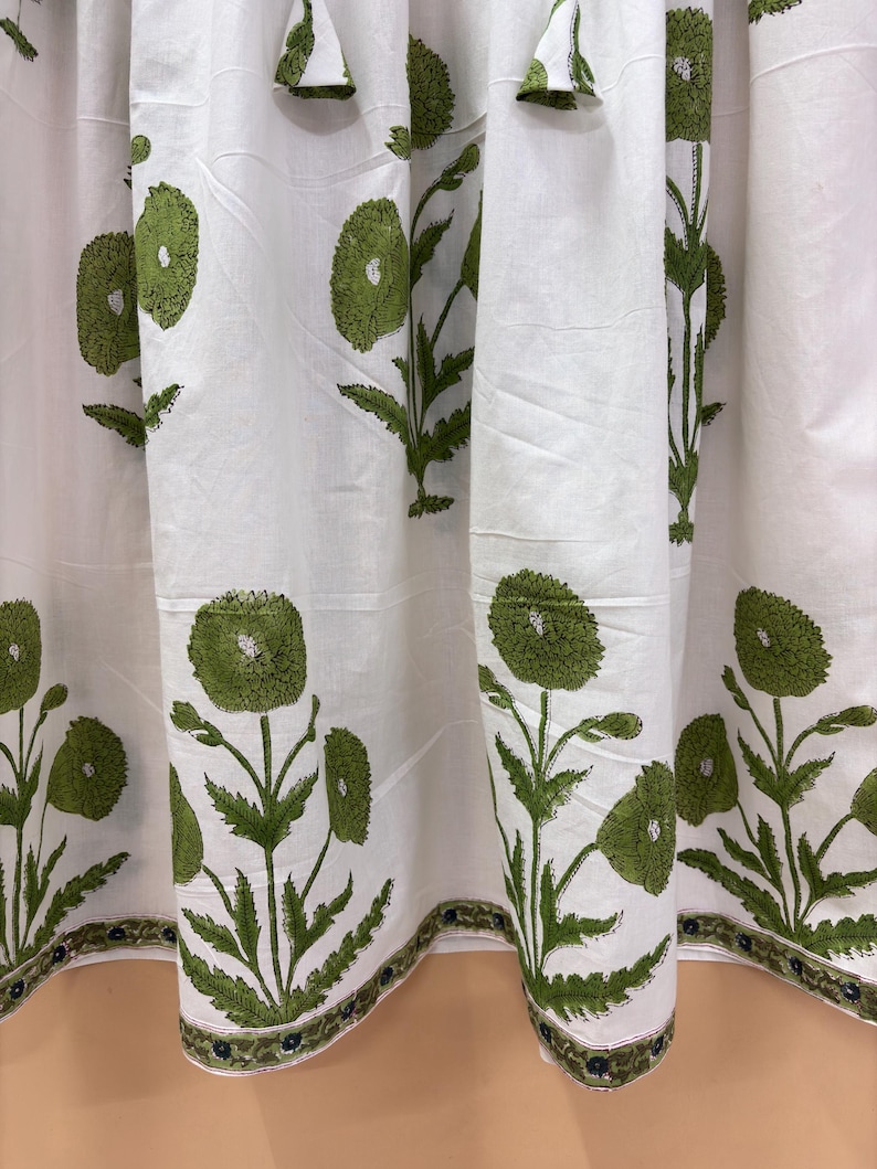 Puede incluir: Tela blanca con un patr&oacute;n repetido de dise&ntilde;os florales verdes. El dise&ntilde;o incluye flores grandes y redondas y hojas detalladas. La tela tiene un borde con un patr&oacute;n verde y azul y est&aacute; adornada con borlas blancas.