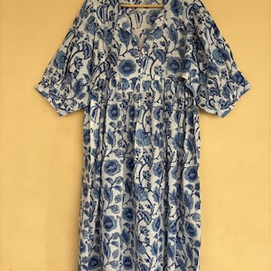 May include: A knee-length dress with a white base and a blue floral pattern. The garment features a split neckline with thin ties, short puff sleeves with gathered cuffs, and a loose, flowing silhouette. A size L tag is visible at the neck.