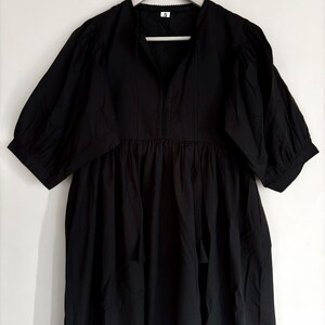May include: A black dress with short, puffed sleeves and a gathered waist. The dress has a V-neckline and a small white tag at the neck. The dress is hanging on a wooden hanger.