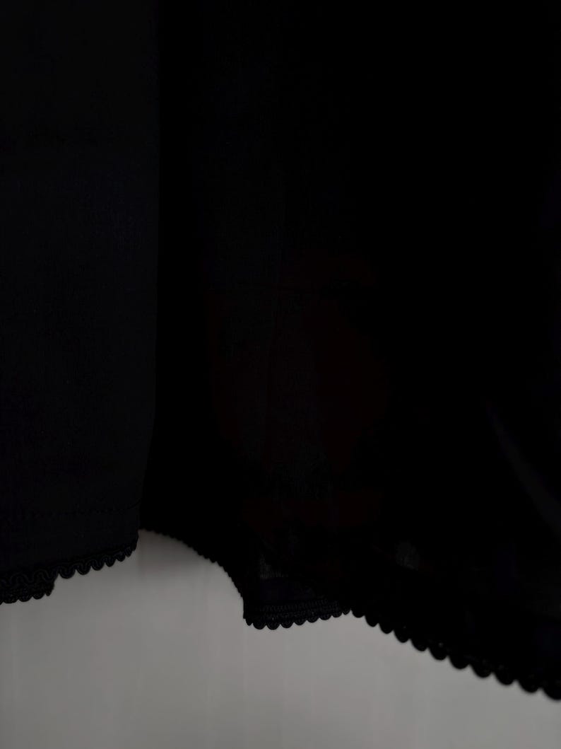 May include: Black underwear with a scalloped lace trim along the edges. The fabric appears to be a soft, opaque material. The image is a close-up of the garment.