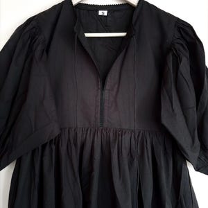 May include: A black dress with a V-neckline and short, puffed sleeves. The dress features a gathered waist and a small, decorative trim around the neckline. The dress is hanging on a wooden hanger.