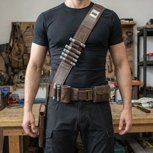 May include: A brown leather utility belt with multiple pouches, a holster, and a shoulder strap. The belt features silver-colored cylindrical accents and a rectangular buckle. The person is wearing a black t-shirt and black cargo pants.