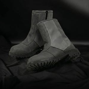 May include: A pair of gray ankle boots with a rugged, treaded sole. The boots have a zipper closure and are made of a textured material. The boots are displayed on a dark background.