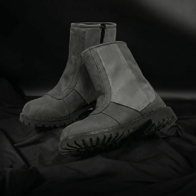 May include: A pair of gray ankle boots with a rugged, treaded sole. The boots have a zipper closure and are made of a textured material. The boots are displayed on a dark background.