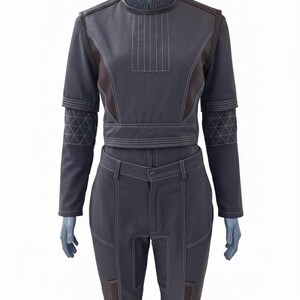 May include: A dark gray two-piece outfit displayed on a mannequin. The top has a high collar, short sleeves, and brown accents. The pants are high-waisted with a button closure and brown patches at the knees. White stitching details the seams.