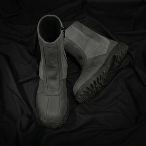 May include: A pair of gray leather boots with a rugged sole. The boots have a mid-calf height, a zipper closure, and a padded collar. The boots are designed for outdoor wear and have a durable construction.