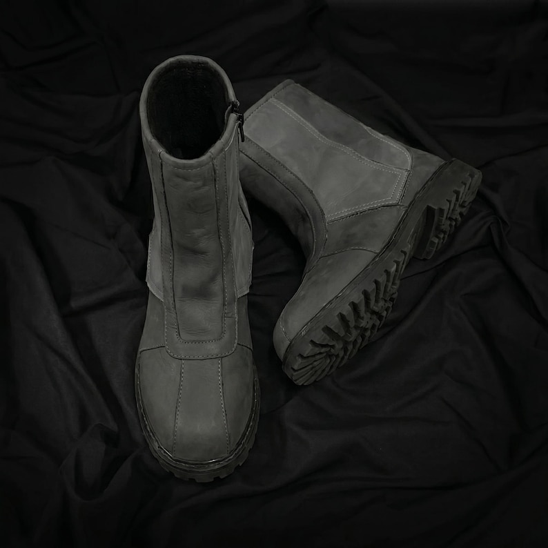 May include: A pair of gray leather boots with a rugged sole. The boots have a mid-calf height, a zipper closure, and a padded collar. The boots are designed for outdoor wear and have a durable construction.