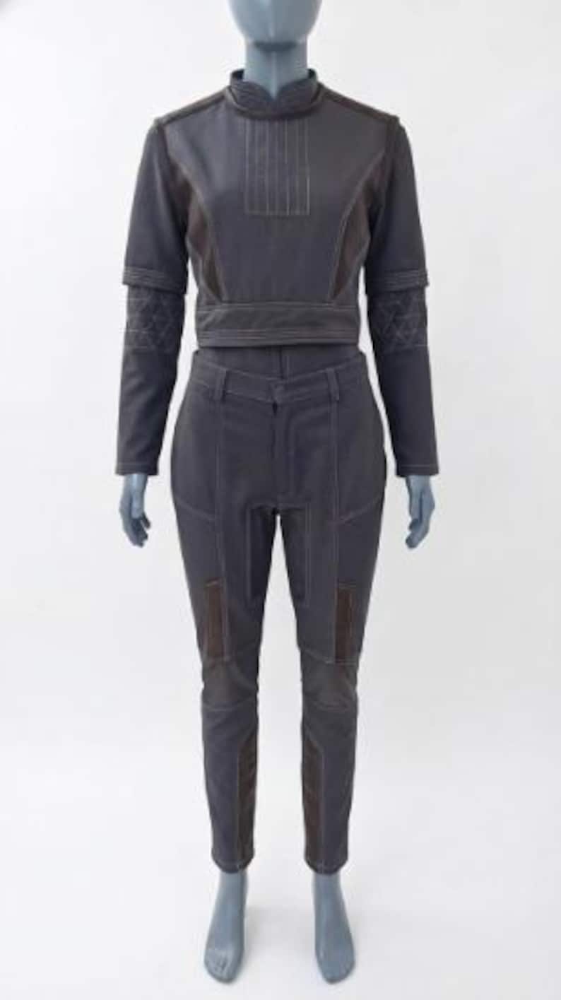 May include: A two-piece outfit in dark gray, featuring a cropped jacket with a high collar and long sleeves, paired with matching pants. The jacket has decorative stitching and brown accents. The pants have brown patches on the knees.