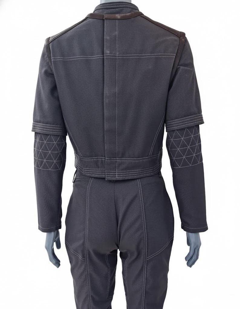 May include: A dark gray jumpsuit with white stitching details. The jacket has a cropped design with geometric patterns on the sleeves. The pants are fitted, and the outfit has a structured, tailored appearance.