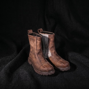K&ouml;nnte beinhalten: Ein Paar braune Lederstiefel mit einem robusten, abgenutzten Aussehen. Die Stiefel haben eine mittlere Wadenh&ouml;he, einen Rei&szlig;verschluss an der Seite und eine dicke, strukturierte Sohle. Das Leder hat ein Used-Finish.