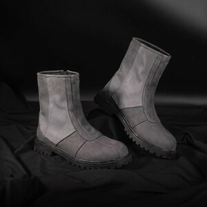 May include: A pair of gray ankle boots with a zipper closure. The boots have a two-tone design, with a lighter gray upper and a darker gray lower section. The soles are black and have a rugged tread.