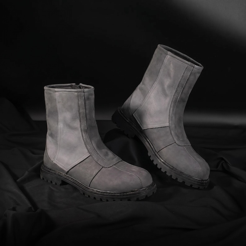May include: A pair of gray ankle boots with a zipper closure. The boots have a two-tone design, with a lighter gray upper and a darker gray lower section. The soles are black and have a rugged tread.