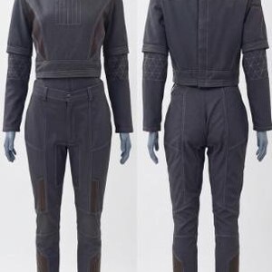 May include: A two-piece dark grey outfit on a mannequin. The top is a cropped jacket with long sleeves and a mandarin collar. The pants are fitted with brown accents. The outfit is made of a sturdy material and features visible stitching.
