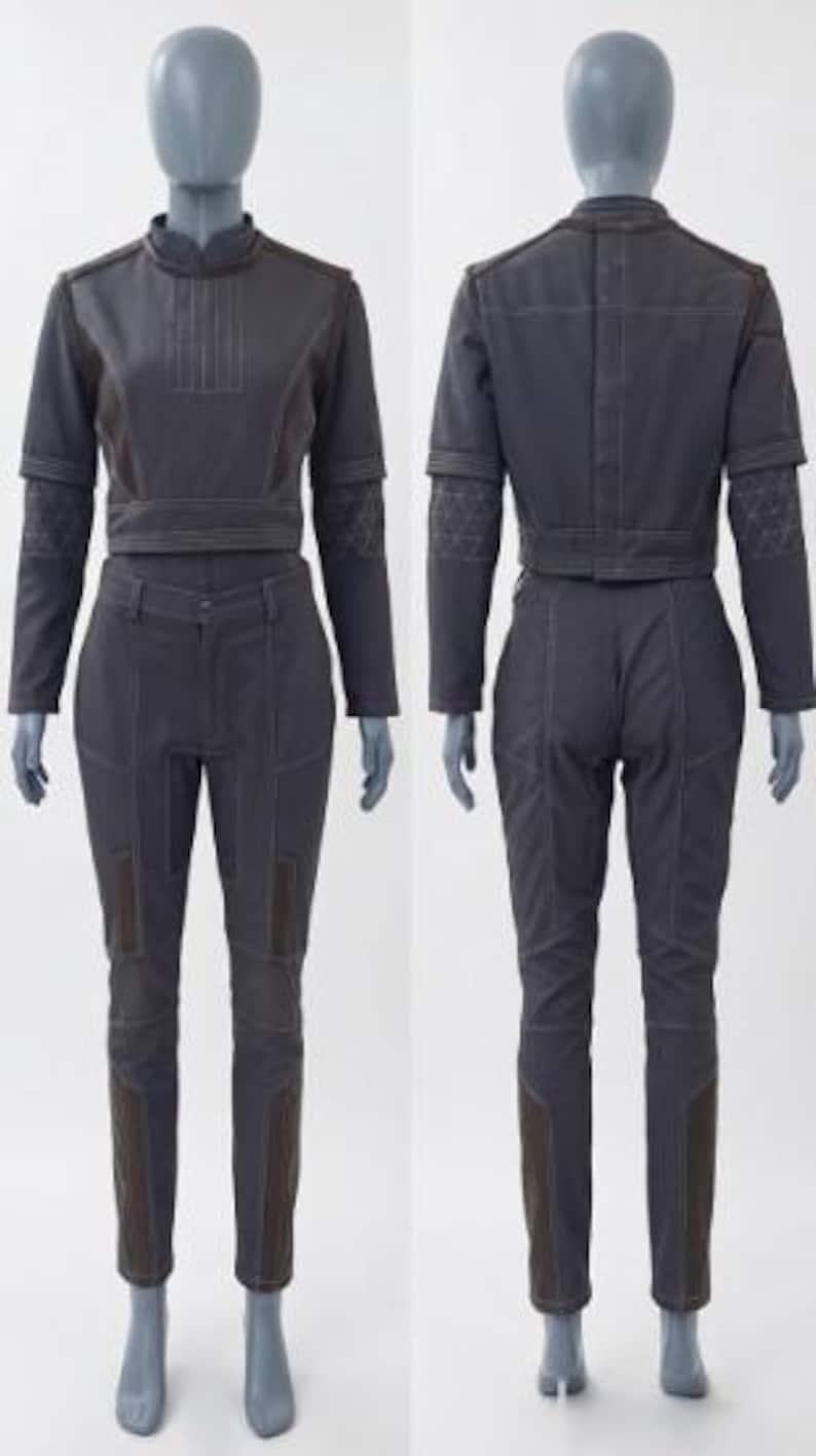 May include: A two-piece dark grey outfit on a mannequin. The top is a cropped jacket with long sleeves and a mandarin collar. The pants are fitted with brown accents. The outfit is made of a sturdy material and features visible stitching.