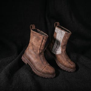 K&ouml;nnte beinhalten: Zwei braune Lederstiefel mit einem Used-Look. Sie haben Rei&szlig;verschl&uuml;sse, Zuglaschen und klobige Sohlen. Ein Stiefel hat einen hellgrauen Einsatz am Schaft. Robuste und stilvolle Schuhe.