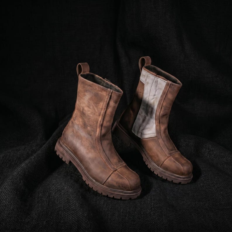 K&ouml;nnte beinhalten: Zwei braune Lederstiefel mit einem Used-Look. Sie haben Rei&szlig;verschl&uuml;sse, Zuglaschen und klobige Sohlen. Ein Stiefel hat einen hellgrauen Einsatz am Schaft. Robuste und stilvolle Schuhe.