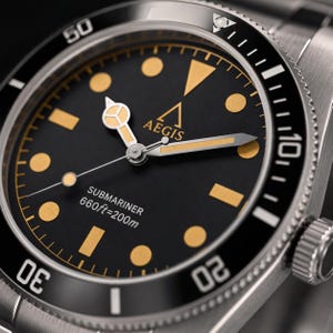 May include: A stainless steel wristwatch with a black dial, gold-toned circular and rectangular hour markers, and gold-toned hands. The dial features the text AEGIS, SUBMARINER, and 660ft=200m. It has a black rotating bezel with white numerals.
