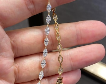 May include: Two gold bracelets featuring a series of marquise-cut clear stones set in a delicate chain. One bracelet displays the stones facing forward, while the other shows the side profile of the settings. A small clasp is visible at the bottom.