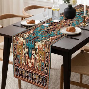 Könnte beinhalten: Ein rechteckiger Tischläufer mit einem detaillierten, farbenfrohen Muster in Türkis, Rot und Gold. Er liegt auf einem dunklen Holztisch, der mit Tellern, Besteck und einem Wasserglas gedeckt ist. Eine Vase mit weißen Blumen und eine Kerze ergänzen das Arrangement.