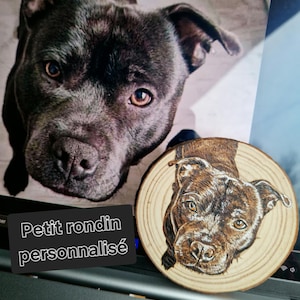 Pode incluir: Um close-up de um cão cinza escuro com olhos castanhos, ao lado de um porta-copos de madeira com um retrato detalhado de um cão semelhante. O porta-copos tem um padrão de grão de madeira natural. O texto em um retângulo preto diz "Petit rondin personnalisé".