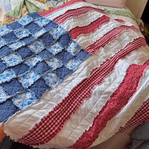 May include: A handmade rag quilt featuring a flag-inspired design. The left section consists of blue squares with white floral and polka dot patterns. The right section features alternating horizontal stripes of white fabric and red gingham.