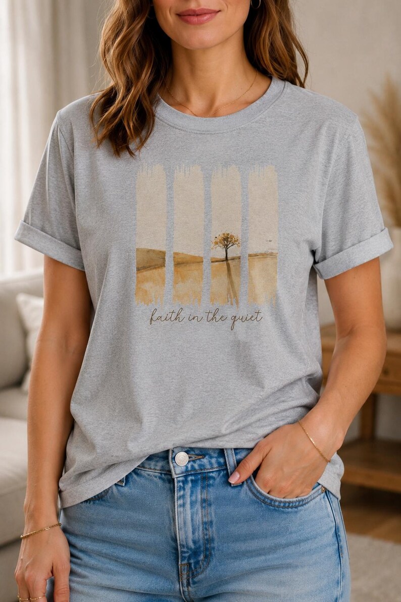 Op de afbeelding: Een lichtgrijs gem&ecirc;leerd t-shirt met korte mouwen en een grafische print van een landschap verdeeld in vier verticale panelen. Het ontwerp toont een goudbruin veld en een enkele boom, met de tekst "faith in the quiet" eronder geschreven.