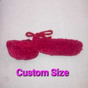 Può includere: Una pantofola all'uncinetto rosa brillante fatta a mano con un fiocco abbinato. La pantofola è realizzata con un filato morbido e strutturato e presenta il testo "Custom Size" in un carattere rosa e viola.