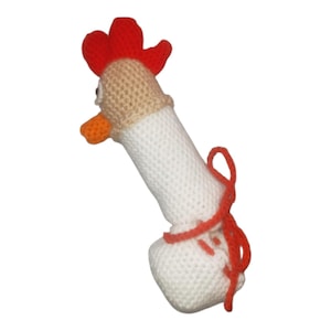 Peut inclure: Un jouet poulet en crochet fait main avec un corps cylindrique blanc, une tête beige, une crête rouge vif et un bec orange. La figurine comprend un cordon en laine rouge noué autour de la partie inférieure, créant un accent visuel sur la base.