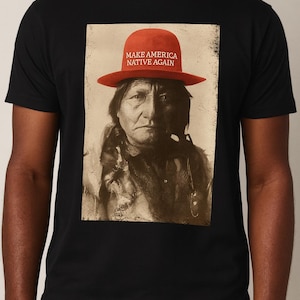 Może przedstawiać: Czarny t-shirt z sepiowym portretem rdzennego Amerykanina w czerwonym kapeluszu. Na kapeluszu widnieje biały napis "MAKE AMERICA NATIVE AGAIN". Koszulka ma okrągły dekolt.