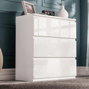 Puede incluir: Cómoda blanca de tres cajones con acabado brillante. Un pequeño reloj que muestra "14 15" y una foto enmarcada se encuentran en la parte superior, junto con un jarrón blanco. La cómoda está contra una pared verde azulado.