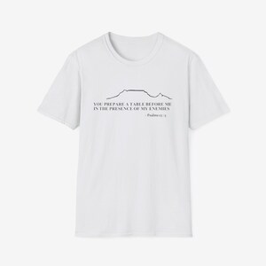Könnte beinhalten: Weißes T-Shirt mit einer schwarzen Bergketten-Grafik und dem Text "YOU PREPARE A TABLE BEFORE ME IN THE PRESENCE OF MY ENEMIES - Psalms 23:5". Das Shirt hat einen Rundhalsausschnitt und kurze Ärmel.