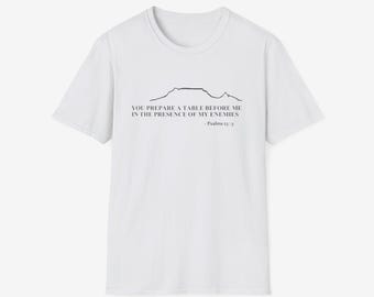 May include: White t-shirt with a black graphic of a mountain range and the text "YOU PREPARE A TABLE BEFORE ME IN THE PRESENCE OF MY ENEMIES - Psalms 23:5". The shirt has a crew neck and short sleeves.