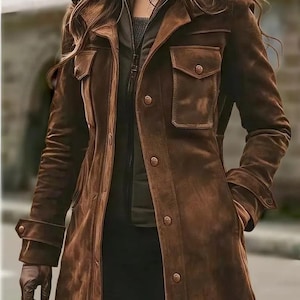 Peut inclure: Un manteau en daim marron avec une fermeture boutonnée, deux poches de poitrine et des manches longues. Le manteau a un design classique et une coupe ajustée. Le manteau est porté sur une veste vert foncé et un pantalon noir.
