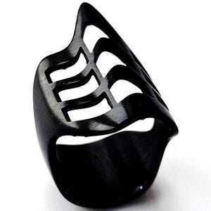May include: A black ring with a unique design. The ring features a series of parallel, curved cutouts along the top, creating an open, geometric pattern. The ring is made of a solid, dark material, and the design is symmetrical.