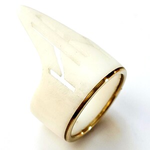 May include: Ivory-colored ring with a pointed, horn-like design. The ring features a gold-colored band and a cut-out design on the ivory portion. The ring is a unique piece of jewelry.