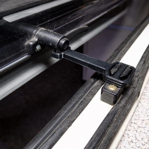 Könnte beinhalten: Nahaufnahme eines schwarzen Verriegelungsmechanismus, wahrscheinlich für ein Fahrzeug. Der Riegel ist an einem weißen und schwarzen Rahmen befestigt, mit einer sichtbaren Schraube und einem dunklen Innenraum.