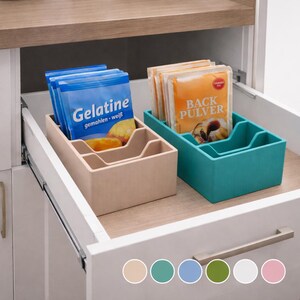 Könnte beinhalten: Ein beigefarbener und ein türkisfarbener rechteckiger Schubladen-Organizer mit jeweils drei Innenfächern. Der beige Behälter enthält blaue Päckchen mit der Aufschrift Gelatine, der türkisfarbene Behälter orange Päckchen mit der Aufschrift Back Pulver.