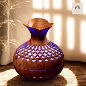 May include: A wooden essential oil diffuser with a vase-like shape. The dark brown body has a pattern of cut-out shapes that emit a soft blue light. The diffuser has a wooden top and sits on a brown woven surface.