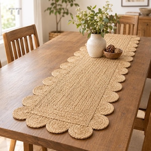 May include: A rectangular table runner made of braided natural tan fibers featuring a scalloped edge design. The runner has a flat, woven center panel surrounded by a border of circular, braided loops that create a decorative, wavy perimeter.