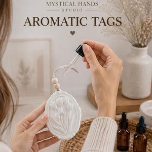 May include: A white oval aromatic tag featuring a raised tulip floral design, suspended by a string with a wooden bead. A glass dropper is positioned above the tag. Text reads: MYSTICAL HANDS STUDIO AROMATIC TAGS. Two amber glass bottles are nearby.