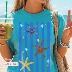 May include: A turquoise t-shirt with a beach theme. The shirt features a design of blue stripes and starfish in purple, orange, and yellow. The text "Lagoon Blue" is visible on the shirt.